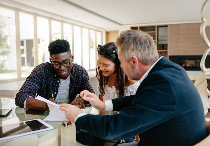 Three people engaged in discussion around a table, reviewing documents in a well-lit modern room. They appear focused and collaborative, suggesting a meeting regarding important aspects of their work or project.