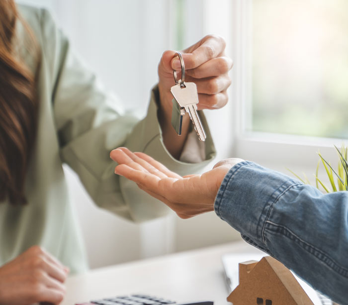 A person handing over house keys to another individual, symbolizing a real estate transaction or property ownership transfer.
