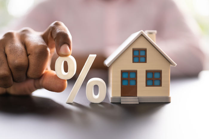 Hand holding percentage symbol next to a small model house, representing interest rates in housing finance.